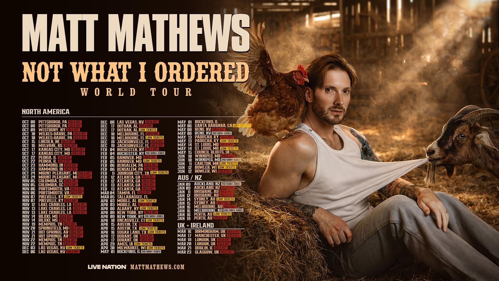 Matt Mathews in a white vest and light trousers seated in a barn, with a chicken and goat beside the Not What I Ordered World Tour lettering.